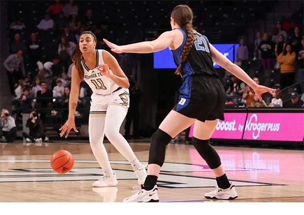 female basketball player bounces basketball while a player from the opposing team guards her